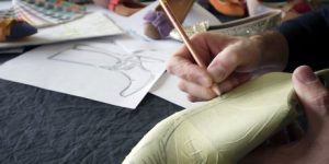 Artisan drawing shoe design pattern on a wooden shoe last