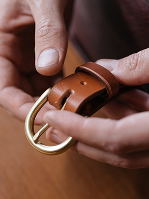 Artisan holding brown leather belt with metal buckle